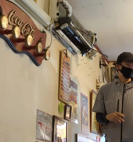 飲食店でエアコンを分解し作業内容を説明しているMINAMOの施工場面